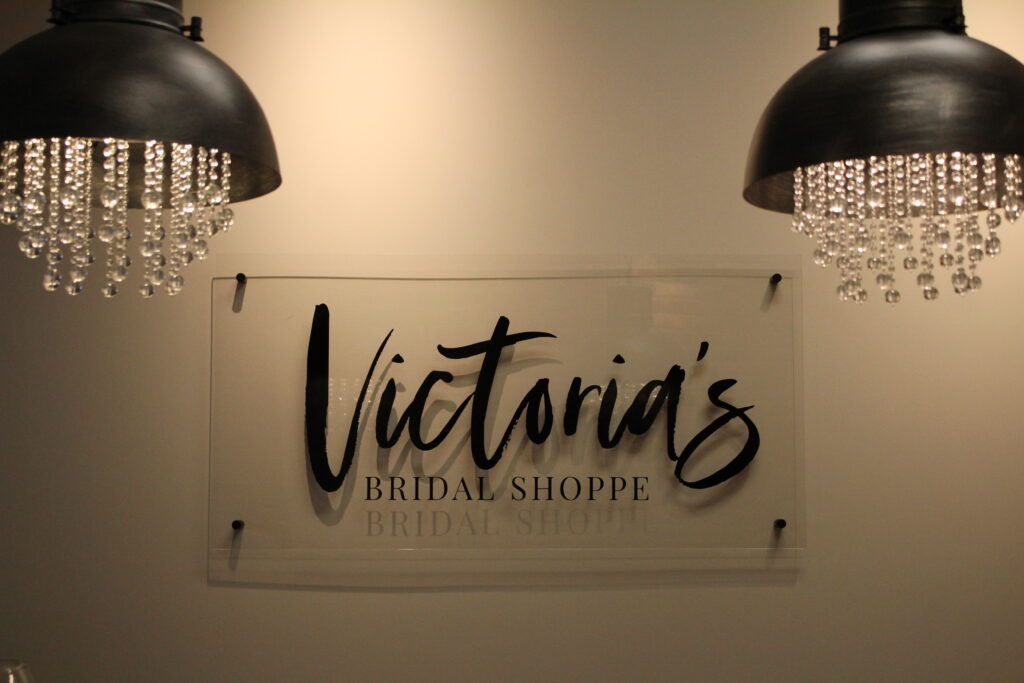 Sign reading "Victoria's Bridal Shoppe" on a wall, framed by two hanging lamps with crystal bead decorations.