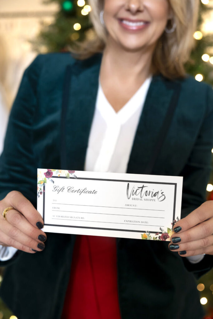 A woman holds a Victoria’s Bridal Shoppe gift certificate in front of a decorated Christmas tree.